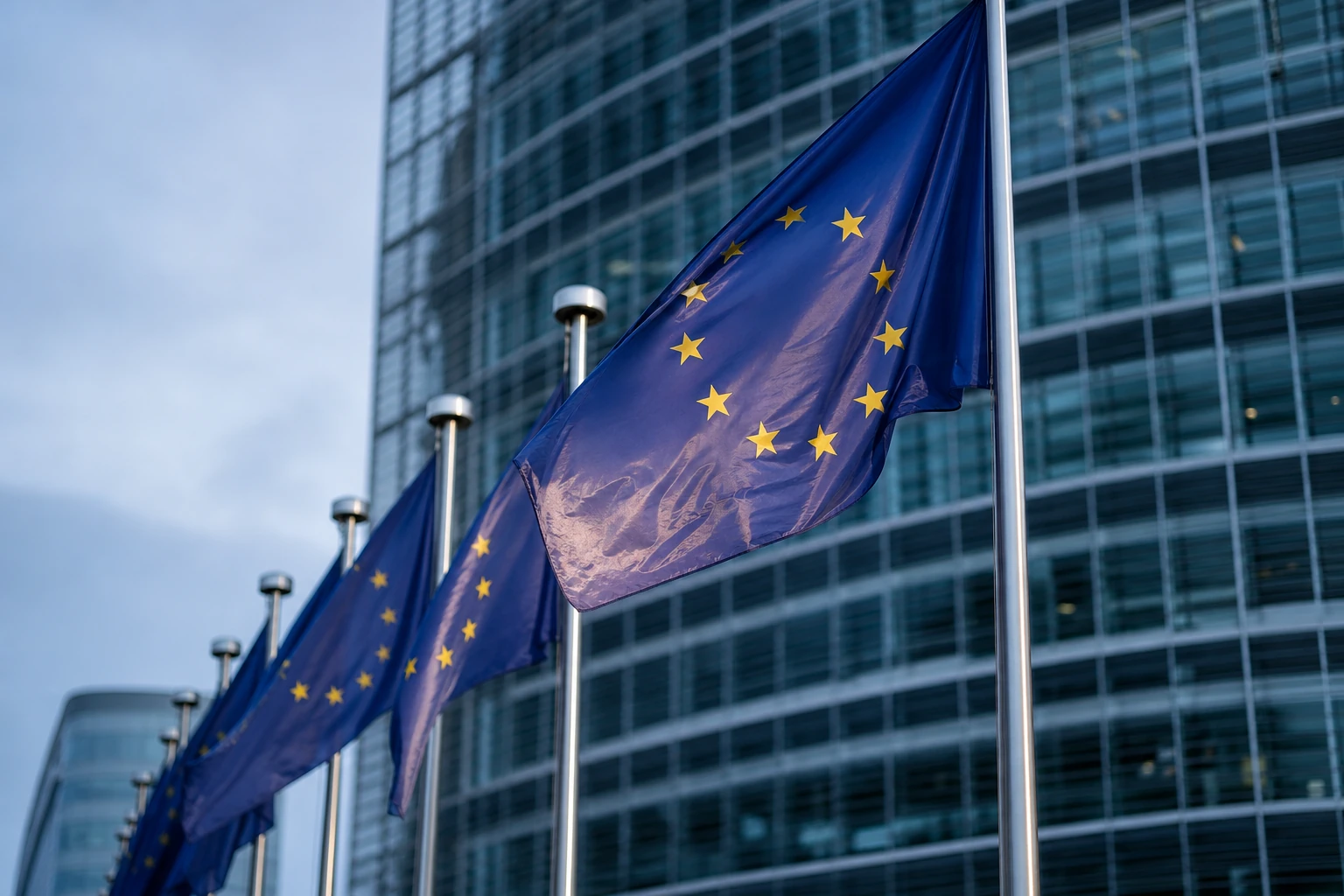 Drapeau européen flottant devant la façade vitrée d'un bâtiment institutionnel bruxellois, au petit matin, arrière-plan volontairement flou